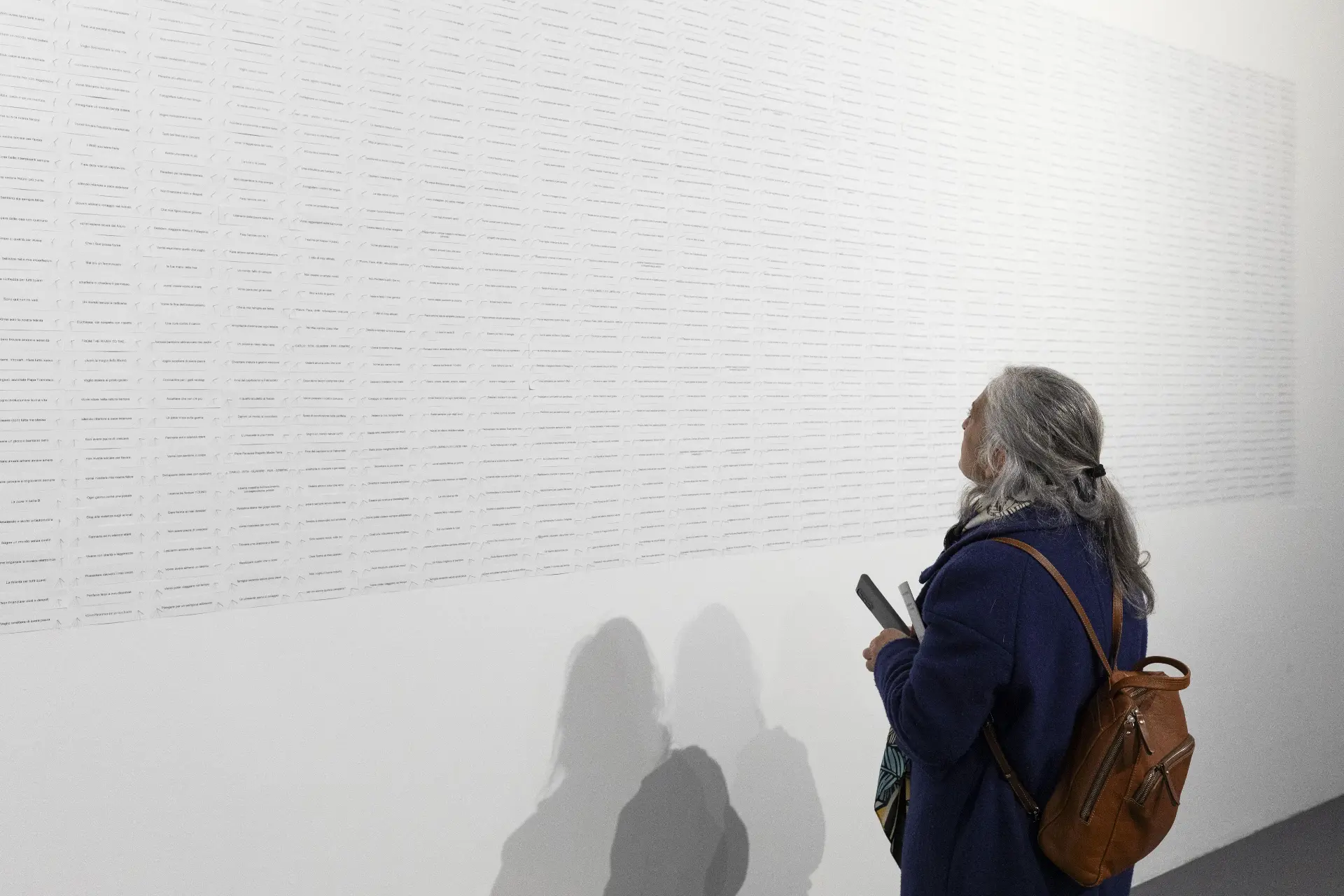 Un desiderio in cinque parole — visitor reading the wall covered with printed wishes