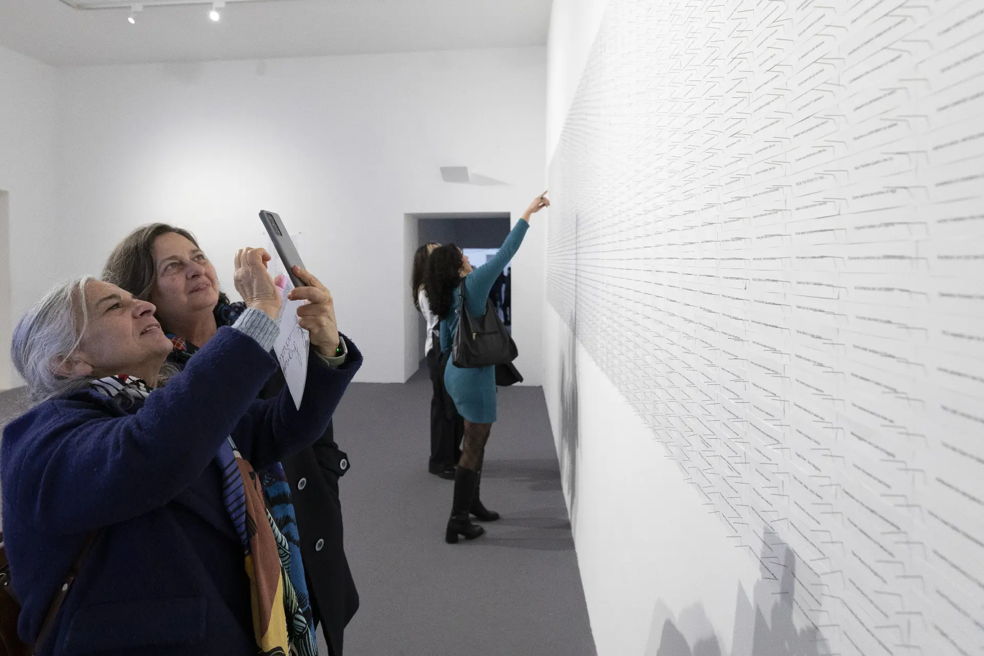 Un desiderio in cinque parole — visitors photographing and pointing at the wall of wishes